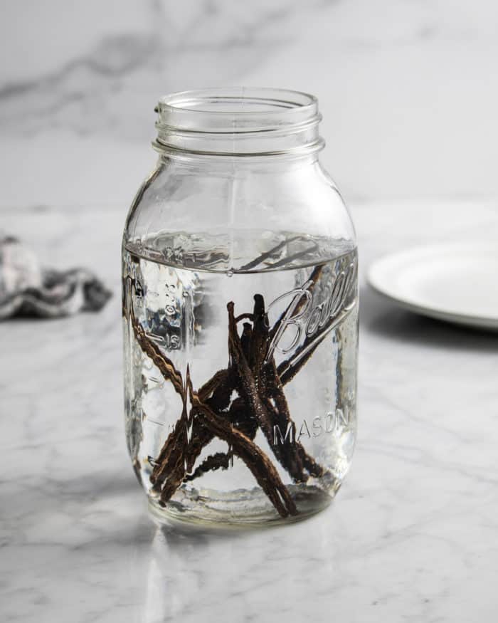 Vanilla beans covered with vodka in a clear glass mason jar.