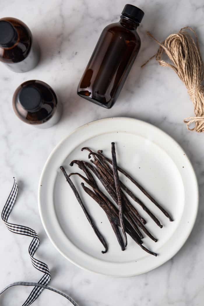 Vanilla beans on a white plate next to small amber bottles.