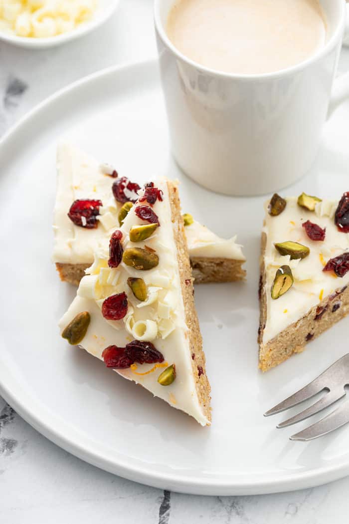 Close up of cranberry bliss bars on a white plate next to a cup of coffee