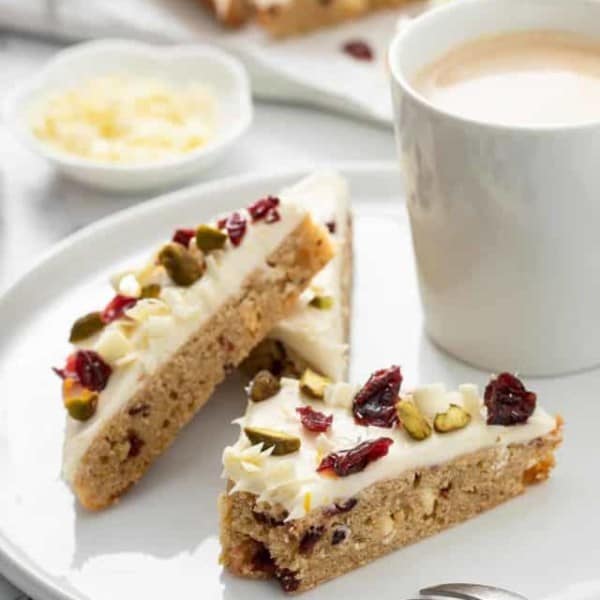 Three cranberry bliss bars arranged on a white plate, with a bite taken out of one of them