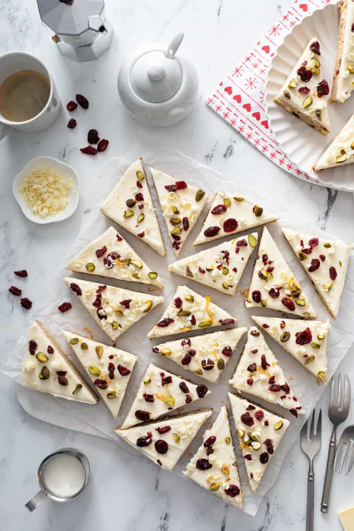 Overhead view of a pan of cranberry bliss bars cut into triangles and topped with cranberries, pistachios, and white chocolate curls