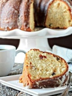 Slice of eggnog cake on a plate in front of a cake stand holding eggnog cake