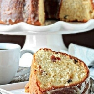 Slice of eggnog cake on a plate in front of a cake stand holding eggnog cake