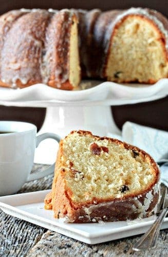 Slice of eggnog cake on a plate in front of a cake stand holding eggnog cake