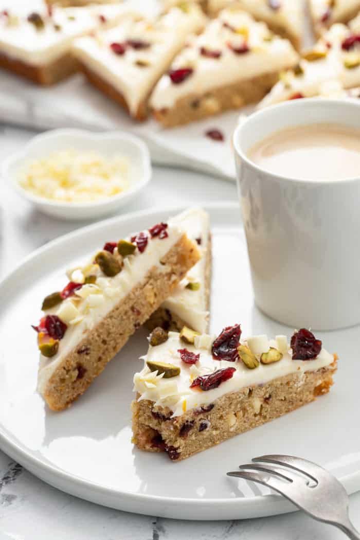 Three cranberry bliss bars arranged on a white plate, with a bite taken out of one of them