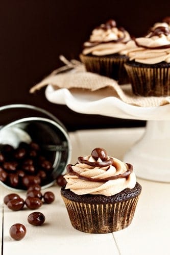 Cafe mocha cupcake in front of a spilled container of chocolate covered espresso beans and a cake stand full of cupcakes