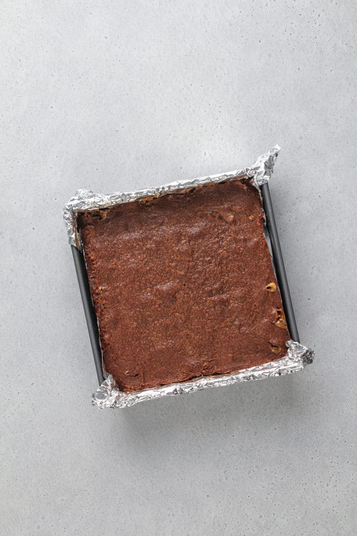 Baked snickers brownies in a foil-lined pan, set on a gray countertop.