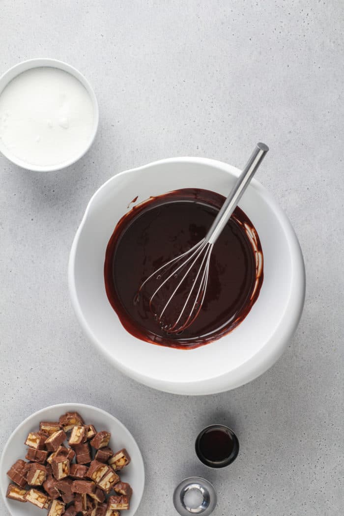 Melted chocolate and butter being whisked in a whit mixing bowl on a gray countertop.