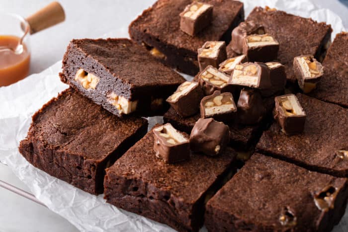 Snickers brownies cut into pieces and topped with pieces of snickers candy bars.