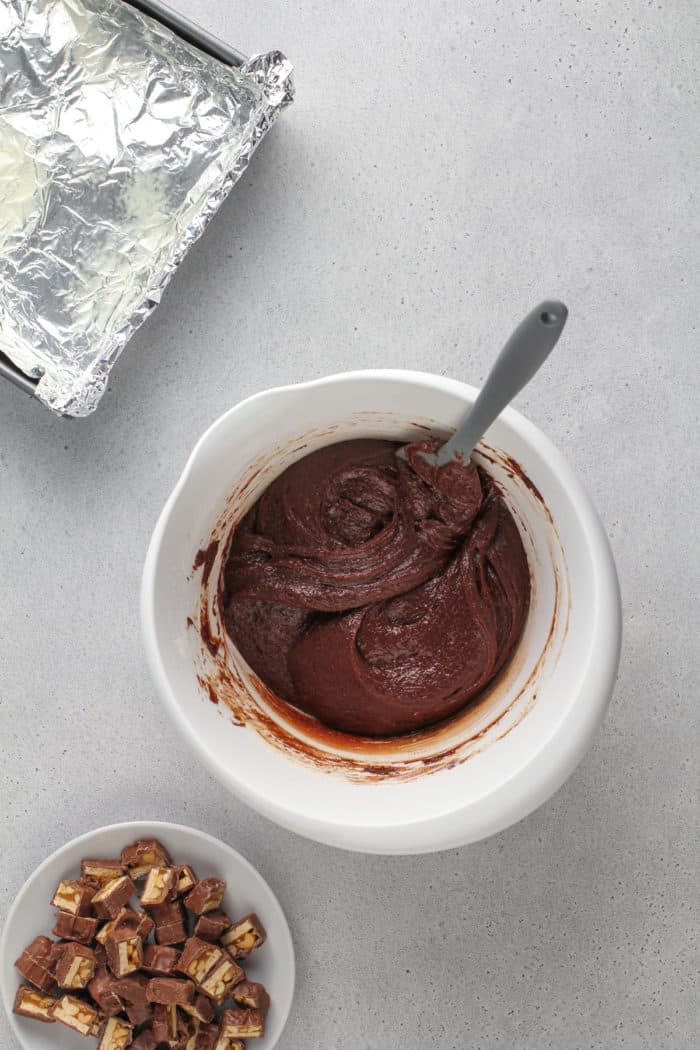 Snickers brownie batter in a white mixing bowl, set on a gray countertop.