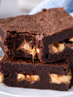 Two snickers brownies stacked on a plate. A bite has been taken out of the corner of the top brownie.