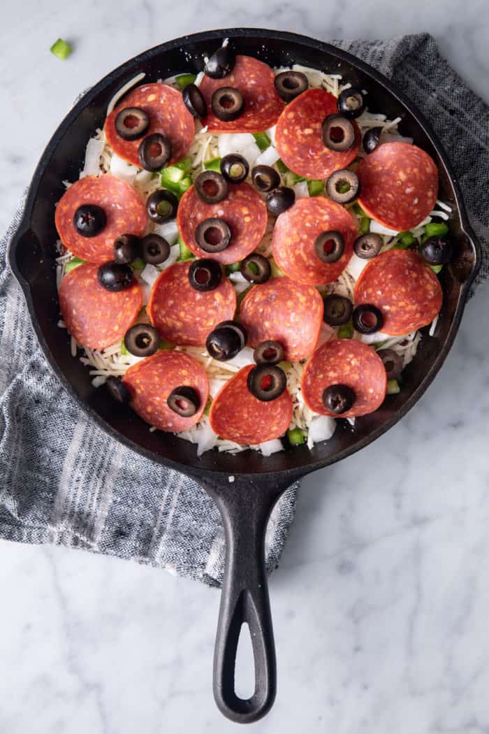 Assembled pizza dip in a cast iron skillet, ready to go in the oven.