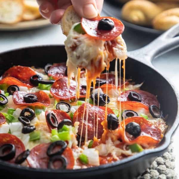 Pizza dip being dipped into with a crostini.