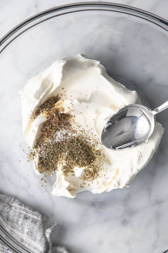 Softened cream cheese and spices in a glass bowl, about to be combined.