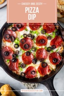 Close up of baked pizza dip with pepperoni, green peppers, and black olives in a cast iron skillet. Text overlay includes recipe name.