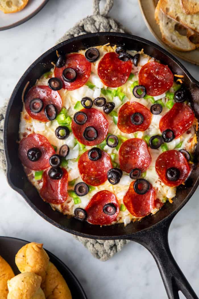 Close up of baked pizza dip with pepperoni, green peppers, and black olives in a cast iron skillet.