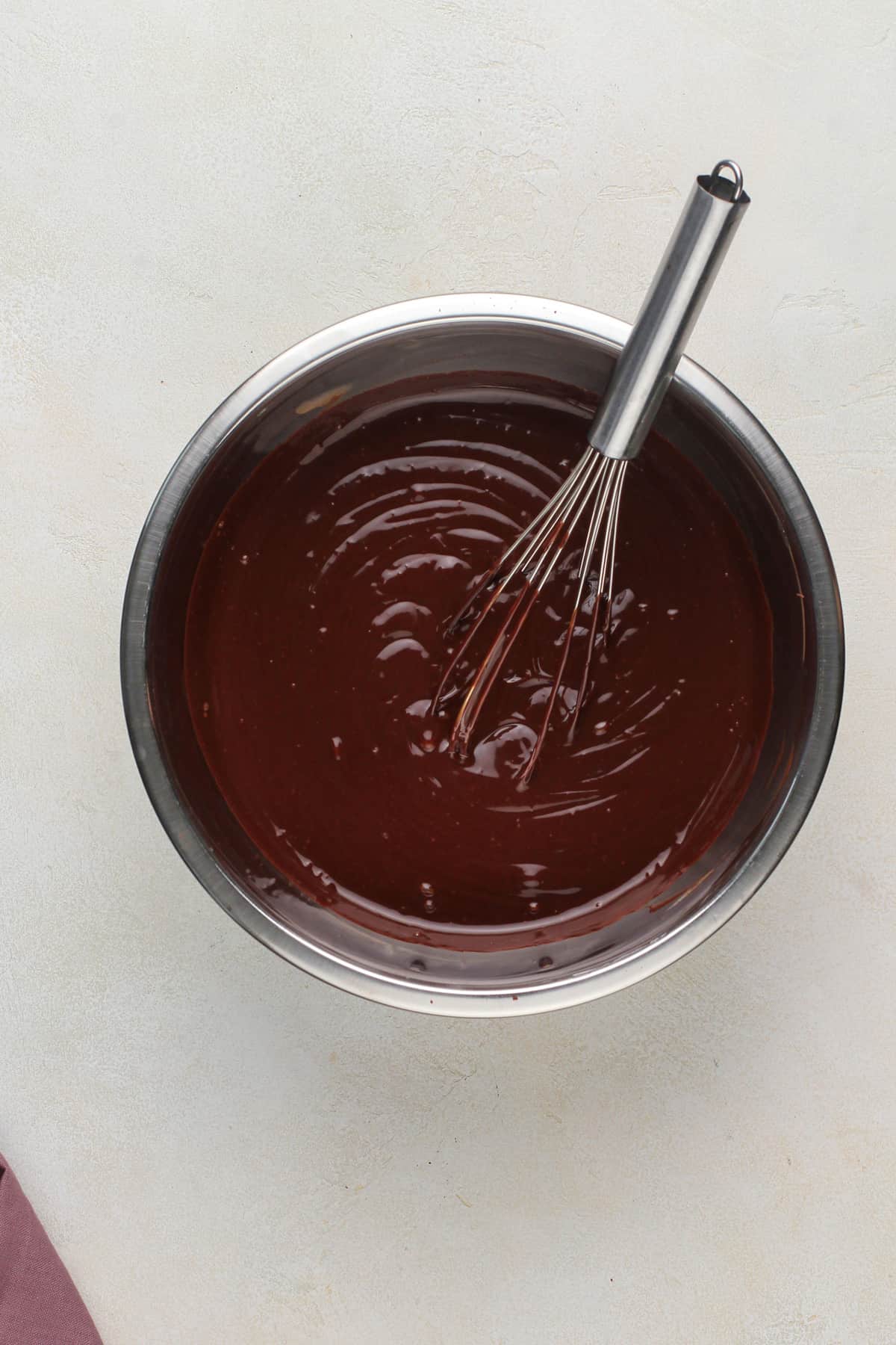 Chocolate ganache being whisked in a metal bowl.