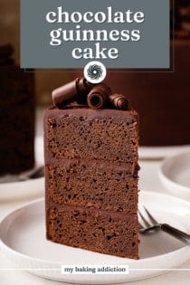 Slice of chocolate guinness cake topped with chocolate curls standing up on a white plate. Text overlay includes recipe name.