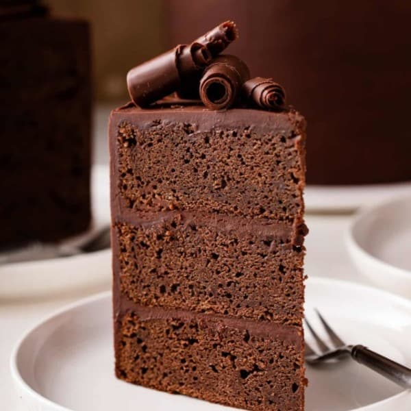 Slice of chocolate guinness cake topped with chocolate curls standing up on a white plate.