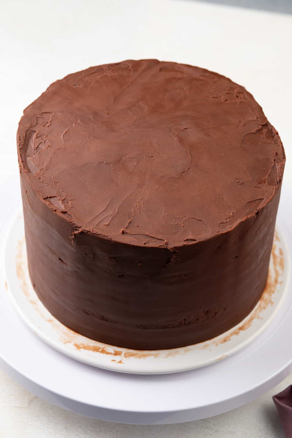 Chocolate guinness cake being coated with chocolate ganache frosting.