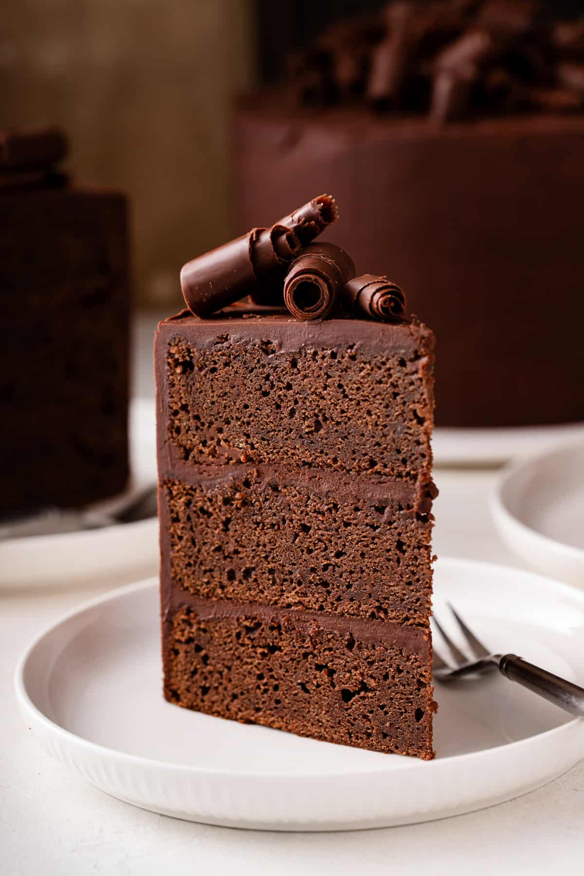 Slice of chocolate guinness cake topped with chocolate curls standing up on a white plate.