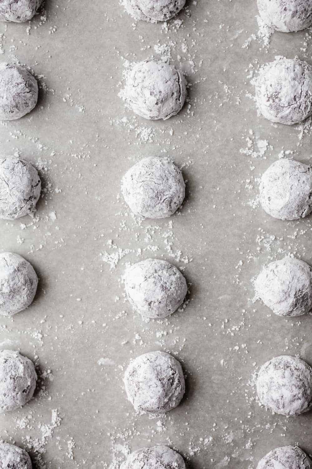 Dough for chocolate crinkle cookies rolled in powdered sugar and arranged on a baking sheet