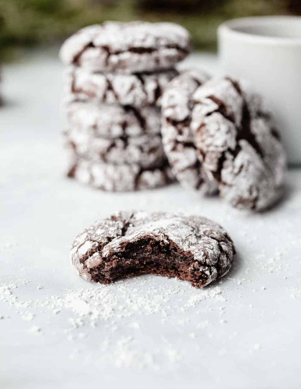 Bite taken out of a chocolate crinkle cookie on a white surface with stacked cookies in the background