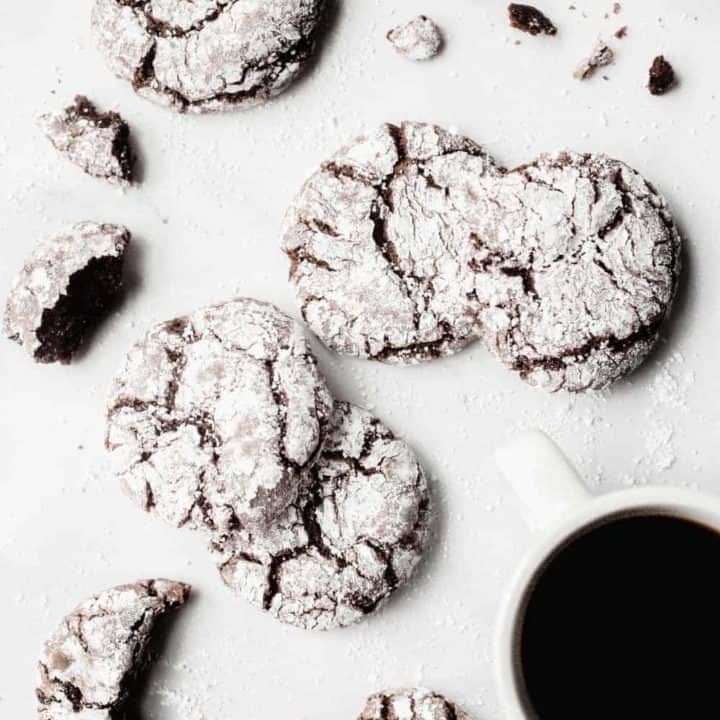 Chocolate crinkle cookies scattered on a white counter with a cup of coffee