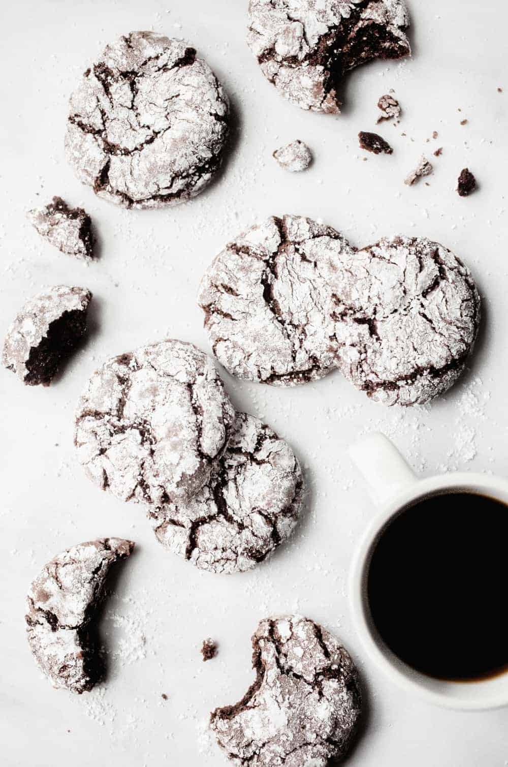 Chocolate crinkle cookies scattered on a white counter with a cup of coffee