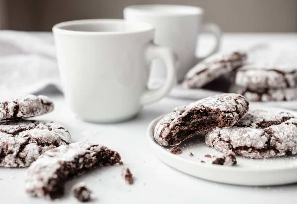 Chocolate crinkle cookies on white plates next to cups of coffee