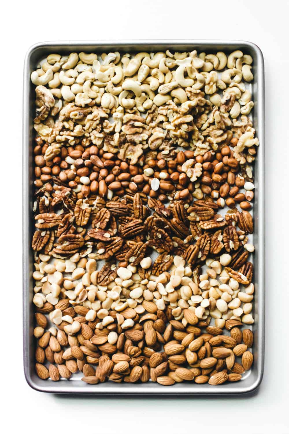 Assorted mixed, toasted nuts arranged on a sheet pan