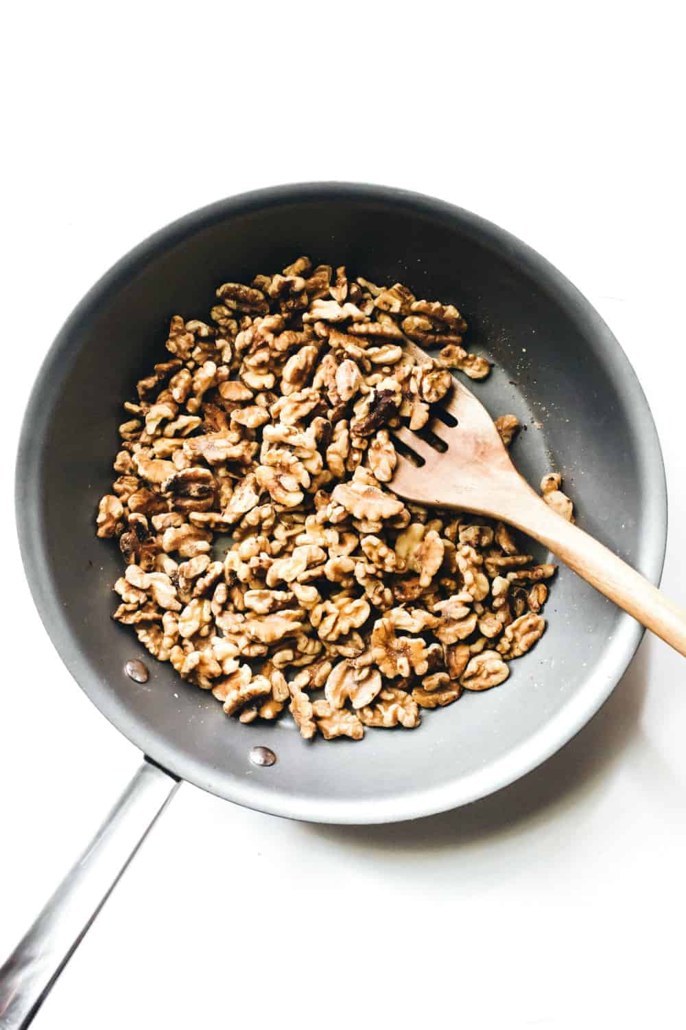 Walnuts in a skillet being stirred with a wooden spoon