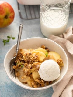 Bowl of apple pear crisp, topped with a scoop of vanilla ice cream, next to a glass of milk