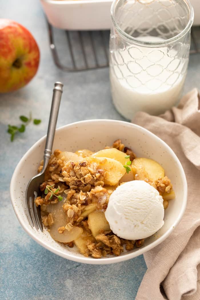 Bowl of apple pear crisp, topped with a scoop of vanilla ice cream, next to a glass of milk