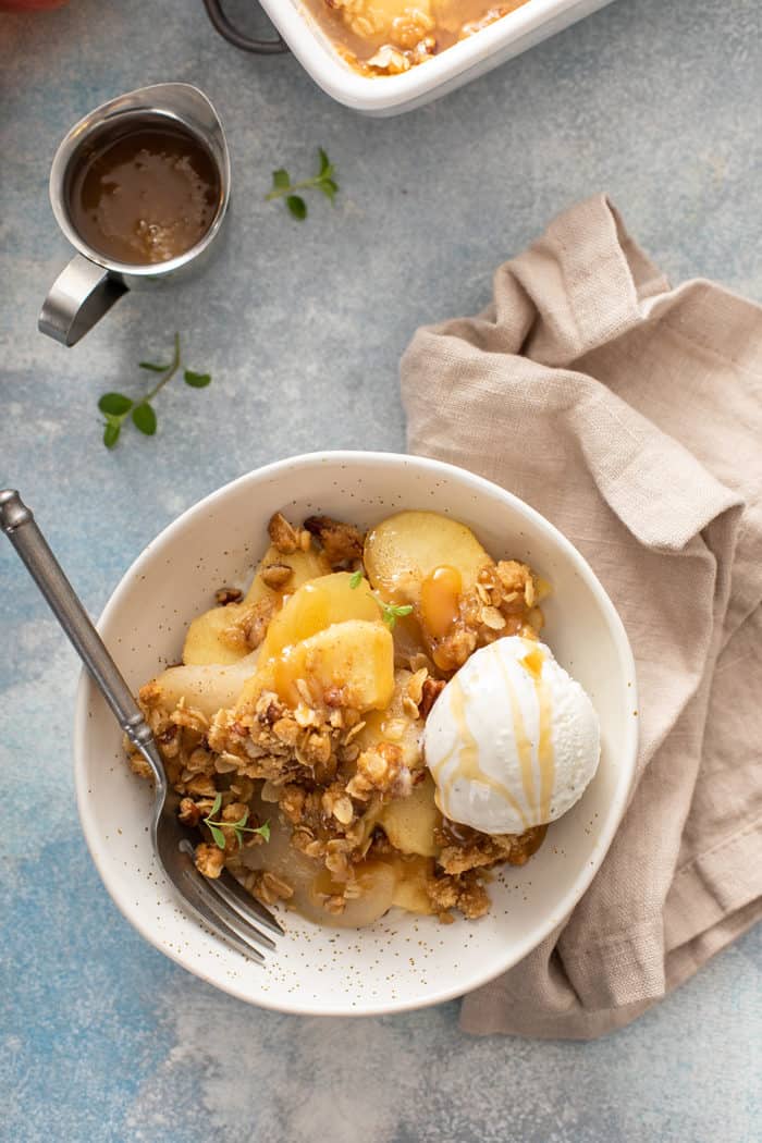 Overhead view of apple pear crisp and vanilla ice cream in a white bowl, drizzled with caramel sauce
