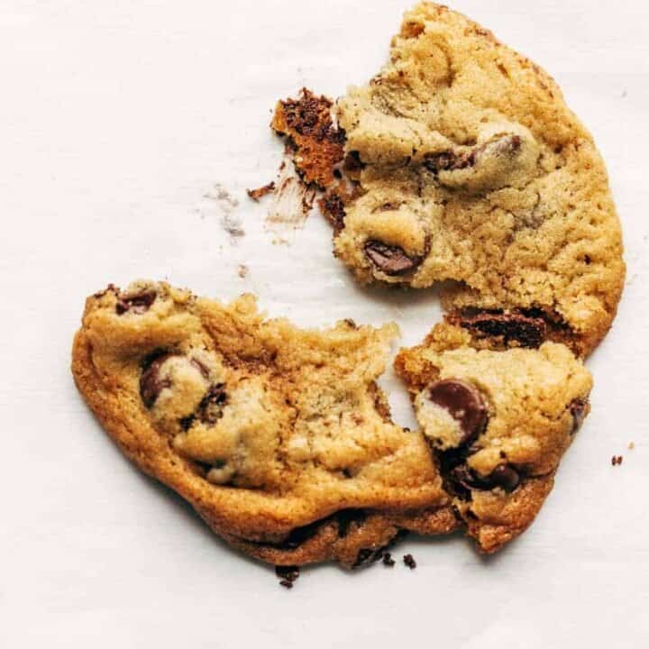Freshly baked chocolate chip cookie broken in half on a white surface