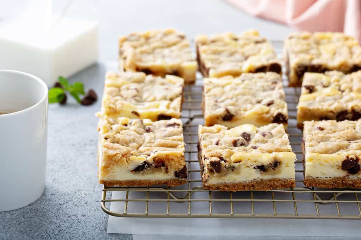 Sliced cookie dough cheesecake bars on a cooling rack over a piece of parchment paper