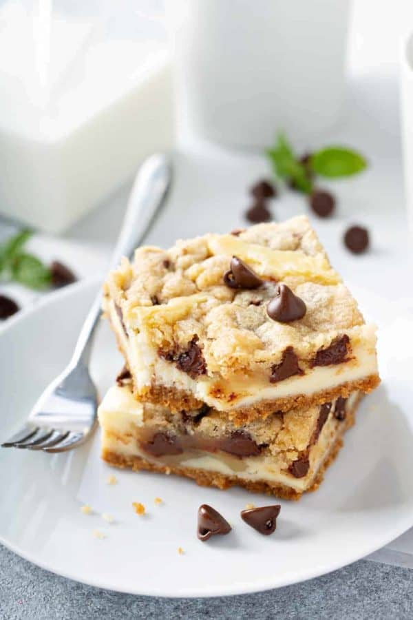 Two plated cookie dough cheesecake bars next to a fork