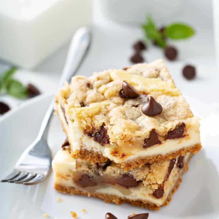 Two plated cookie dough cheesecake bars next to a fork