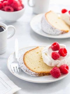 Slice of cream cheese pound cake topping with whipped cream and fresh raspberries next to a fork on a plate