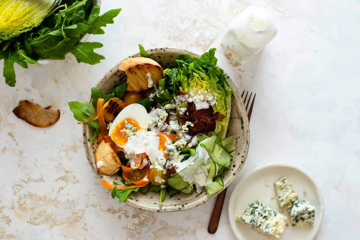 Salad dressed with blue cheese dressing next to blue cheese and a bottle of dressing