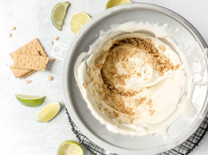 Graham cracker crumbs being folded into key lime pie ice cream in the bowl of an ice cream maker