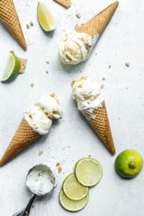 Overhead view of 3 ice cream cones of key lime pie ice cream laying on a marble countertop surrounded by slices of limes