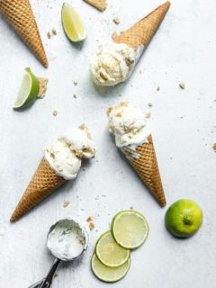 Overhead view of 3 ice cream cones of key lime pie ice cream laying on a marble countertop surrounded by slices of limes