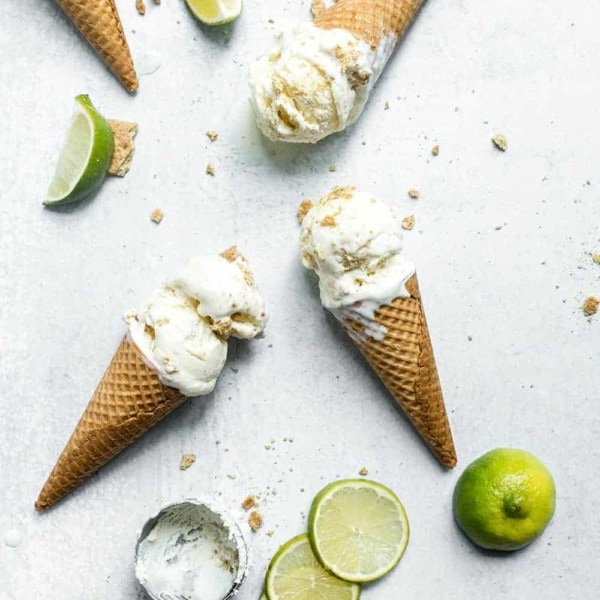 Overhead view of 3 ice cream cones of key lime pie ice cream laying on a marble countertop surrounded by slices of limes