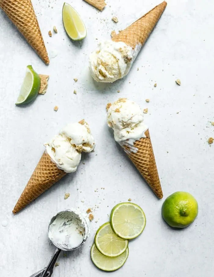 Overhead view of 3 ice cream cones of key lime pie ice cream laying on a marble countertop surrounded by slices of limes