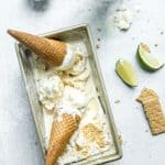 Overhead view of 2 key lime pie ice cream cones set on top of a loaf container of key lime pie ice cream on a marble countertop