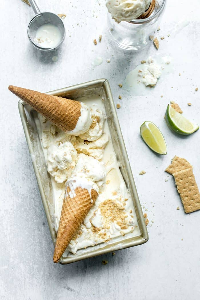 Overhead view of 2 key lime pie ice cream cones set on top of a loaf container of key lime pie ice cream on a marble countertop