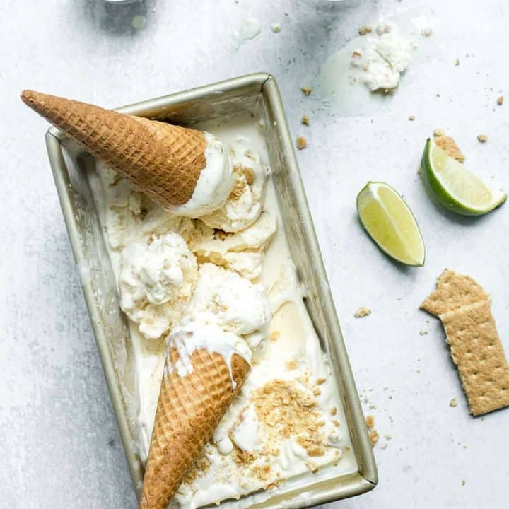 Overhead view of 2 key lime pie ice cream cones set on top of a loaf container of key lime pie ice cream on a marble countertop