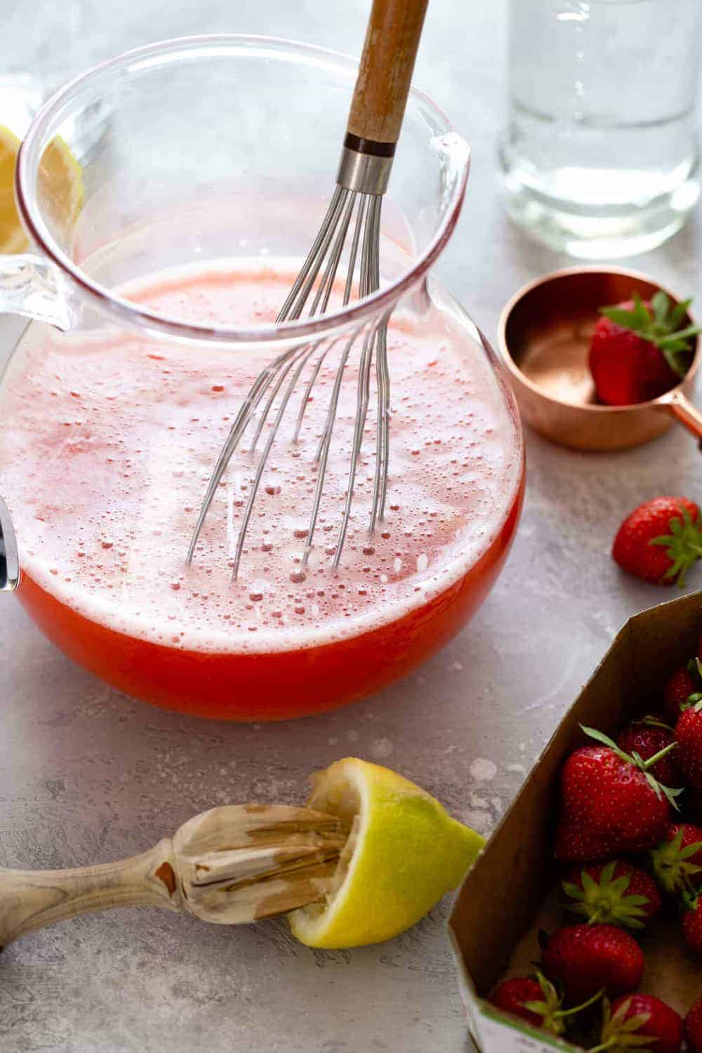 Pitcher of strawberry lemonade being mixed next to lemons and strawberries